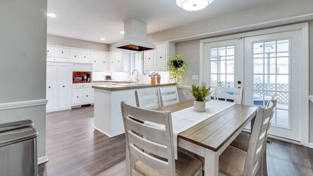 A modern kitchen with white cabinetry, a central island, and a dining area with wooden furniture. - Nancy`s Ranch + hot tub (Derby)