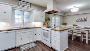 A modern kitchen with white cabinetry, a central island, and a dining area with wooden chairs. - Nancy`s Ranch + hot tub (Derby)