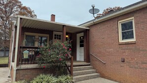 A brick house with a covered porch, a satellite dish, and a small garden with red flowers.