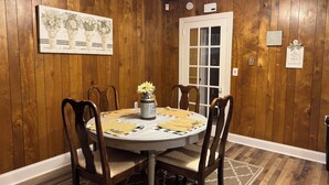 A dining room with a round table, six wooden chairs, a vase with flowers, and a painting on the wall.