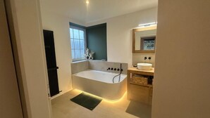 Een moderne badkamer met een vrijstaand bad, een raam, een spiegel en een wastafel.