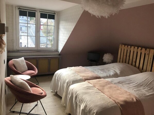 A bedroom with two beds, a chair, a television, and a window with a view of buildings. - Hostellerie de la chapelle (Malmedy)