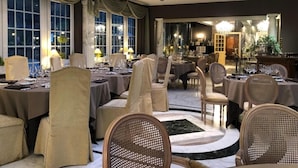 Een ruime, stijlvol ingerichte eetruimte met meerdere tafels en stoelen, grote ramen en een hoge plafond.