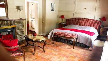 A bedroom with a large bed, a wooden table, a chair, a fireplace, and a door.