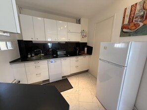 Una cucina con mobili bianchi, un piano di lavoro nero, un frigorifero bianco e un quadro appeso al muro.