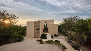 A modern building with a geometric entrance, surrounded by greenery and a sandy path. - KatNap Sisal : Solar-powered Beachfront Retreat (Sisal)