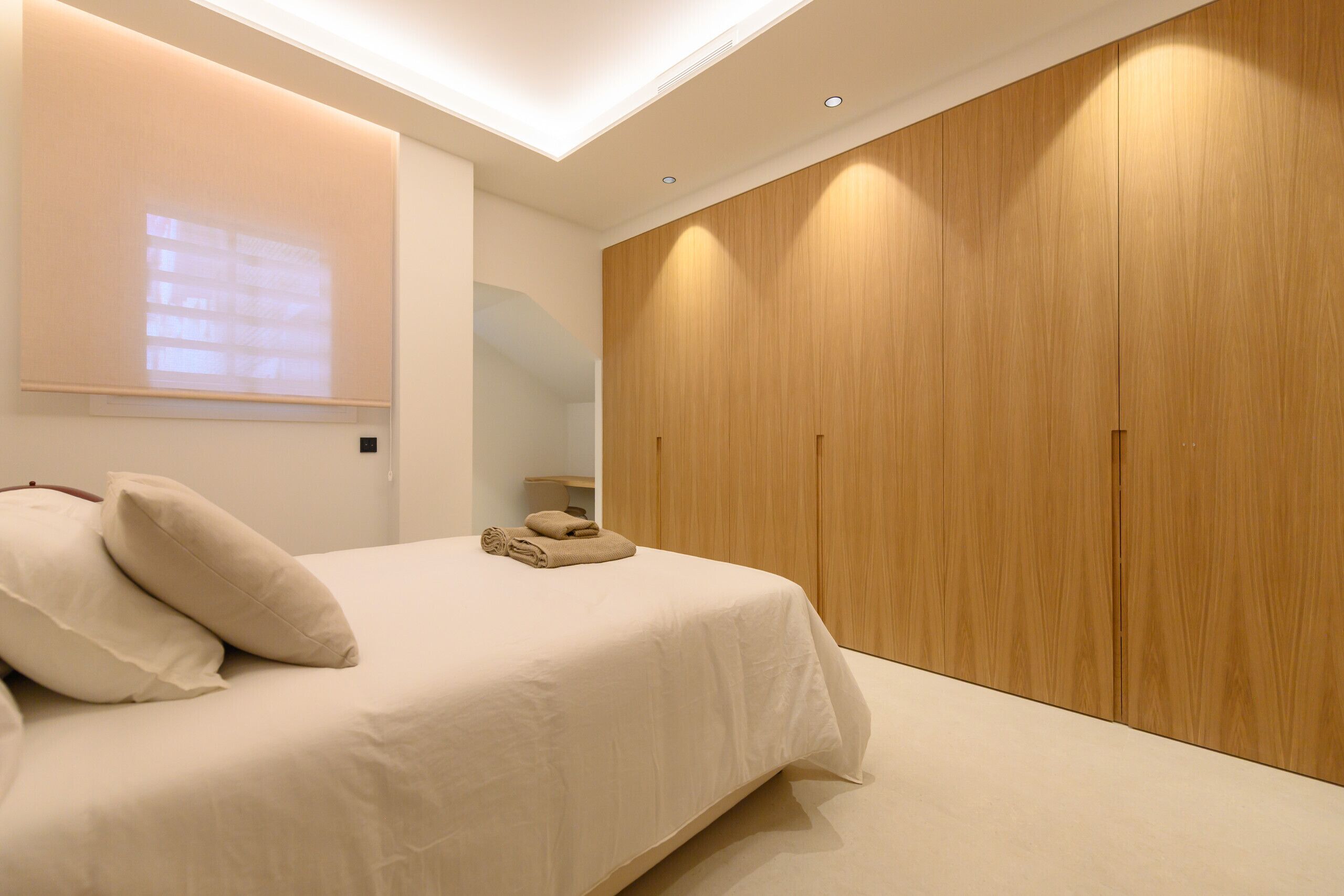 A bedroom with a bed, a wooden wardrobe, and a ceiling light.