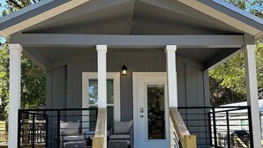 A covered outdoor seating area with a wooden deck, a small porch, and a door leading to the interior. - Brand New Lake Cabin!  1 Mile from Buzzard Roost Boat Dock (Mountain Home)