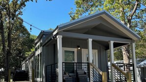 A covered outdoor seating area with a wooden staircase leading up to it, surrounded by trees and a gravel ground. - Brand New Lake Cabin!  1 Mile from Buzzard Roost Boat Dock (Mountain Home)