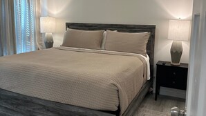 A bedroom with a wooden bed frame, a dark headboard, two bedside tables with lamps, and a window with curtains. - Brand New Lake Cabin!  1 Mile from Buzzard Roost Boat Dock (Mountain Home)