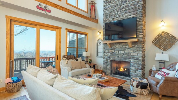 Una sala de estar acogedora con chimenea de piedra, un televisor de pantalla plana grande montado en la pared y un espacio de descanso cómodo con sofá y sillones.