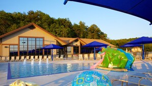 Área de piscina com uma grande escultura de sapo, cadeiras de descanso e guarda-sóis.