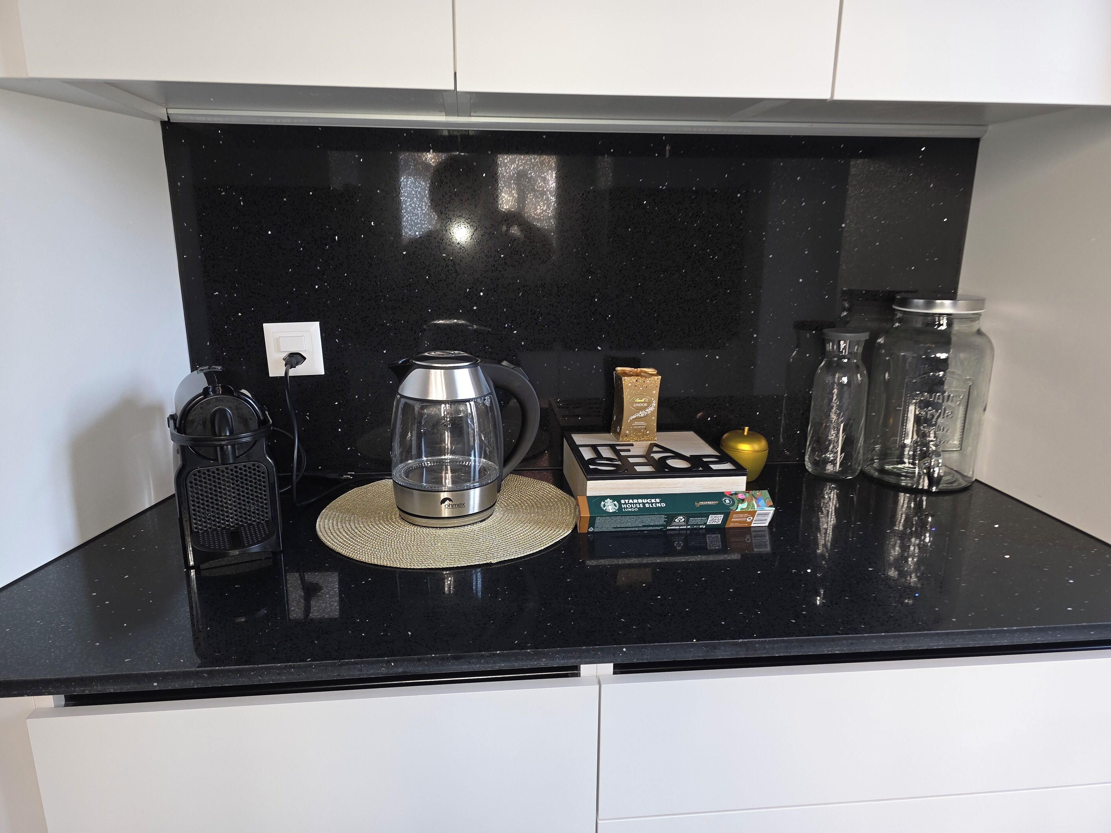 A kitchen counter with a coffee maker, a box of Starbucks House Blend coffee, a gold-colored object, and two glass jars.