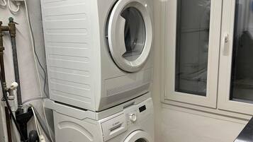 Ein Waschraum mit gestapelten Waschmaschinen, einem Wäscheständer und einem Fenster.