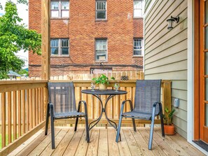 A wooden deck with two chairs and a small table, a brick building in the background, and a wooden fence. - Downtown Suite: Private Fenced Oasis (Asheville)