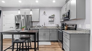 A modern kitchen with grey cabinets, stainless steel appliances, and pendant lighting.