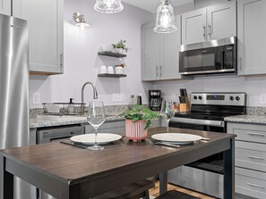 Una cocina moderna con electrodomésticos de acero inoxidable, encimera de granito y una mesa de comedor de madera dispuesta para dos personas.