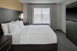 Habitación de hotel con una cama grande, televisor de pantalla plana, ventana con cortinas y vistas al exterior.
