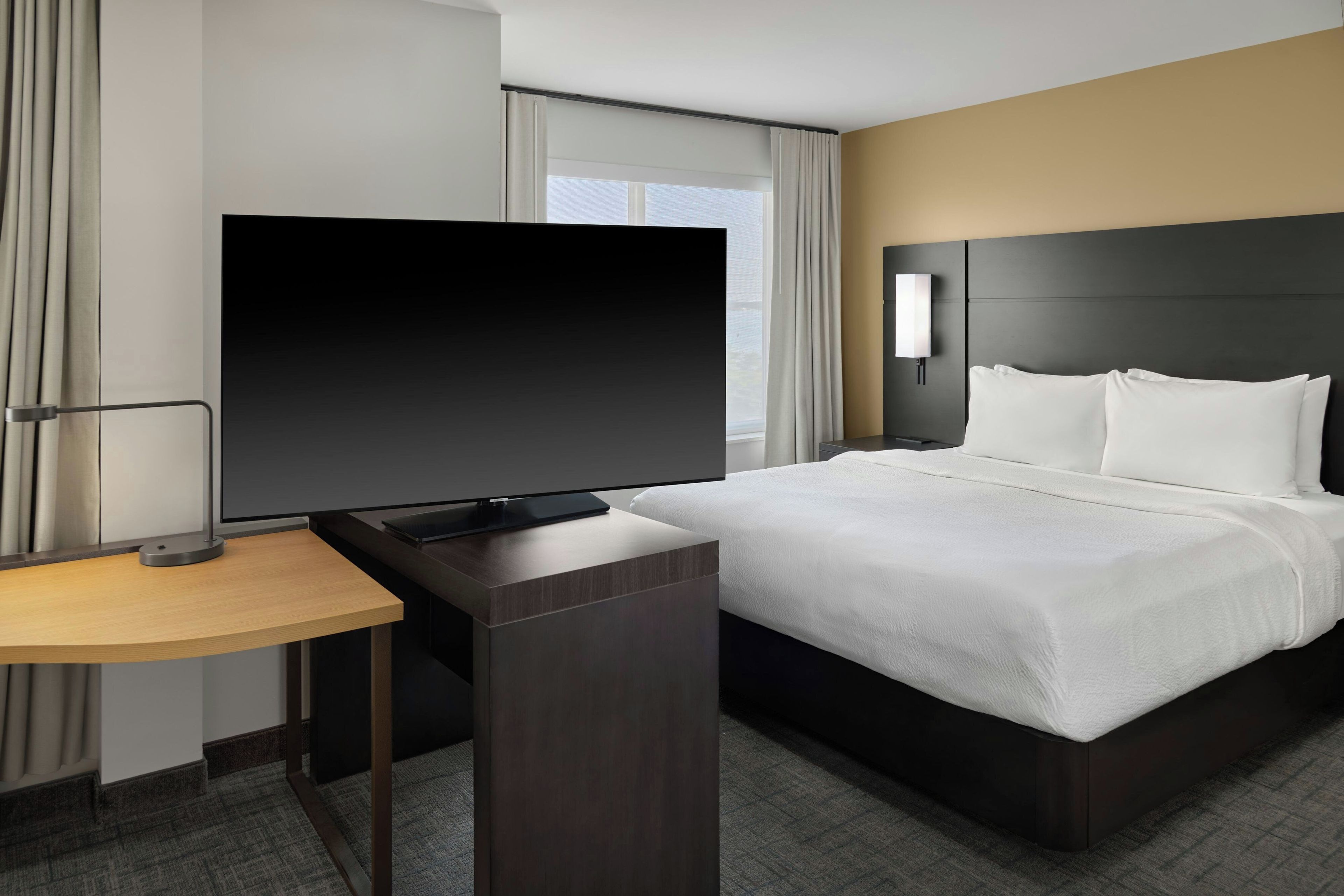 Una habitación de hotel con una cama, televisión, mesita de noche y lámpara.