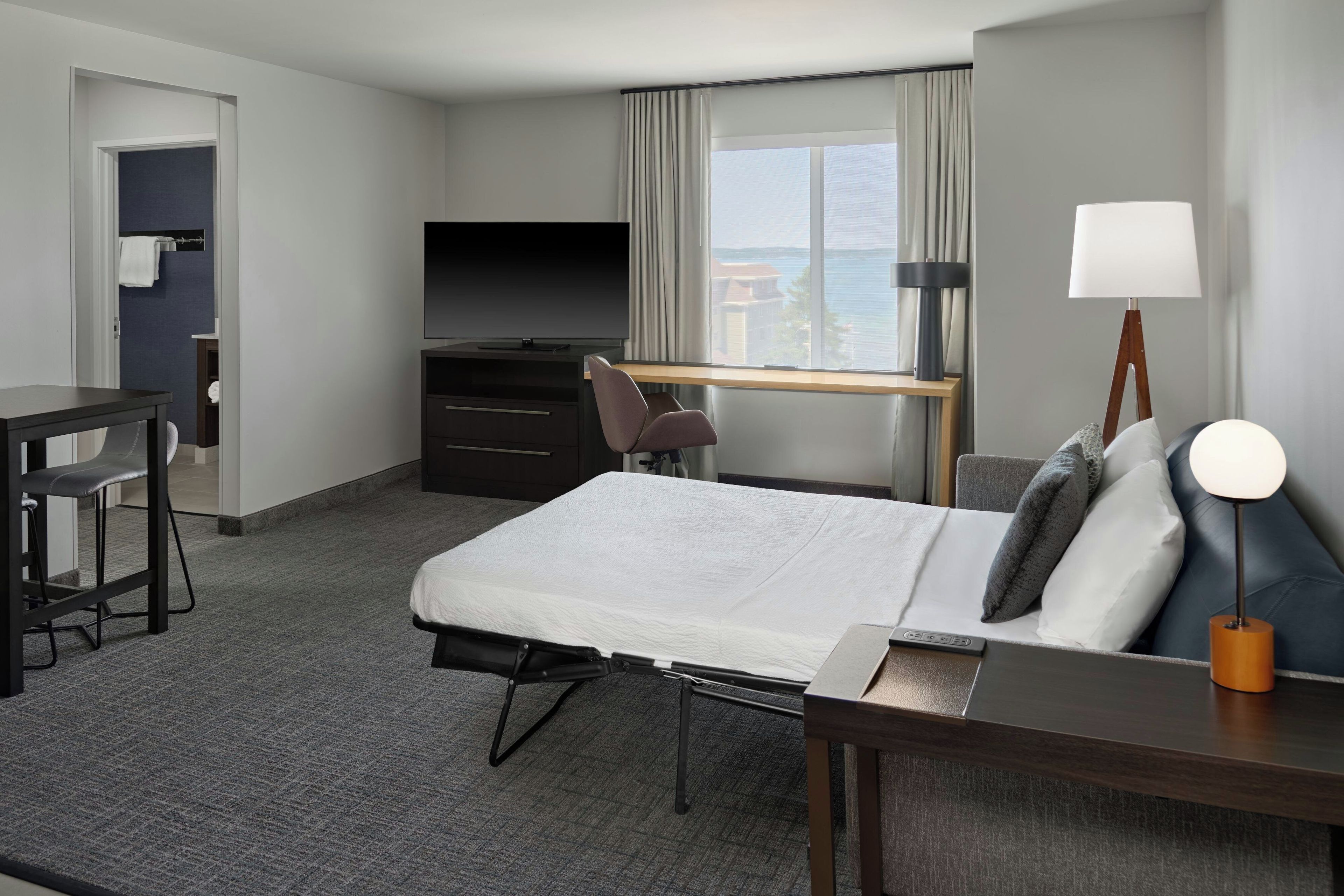 A hotel room with a bed, desk, chair, television, and a view of the sea.