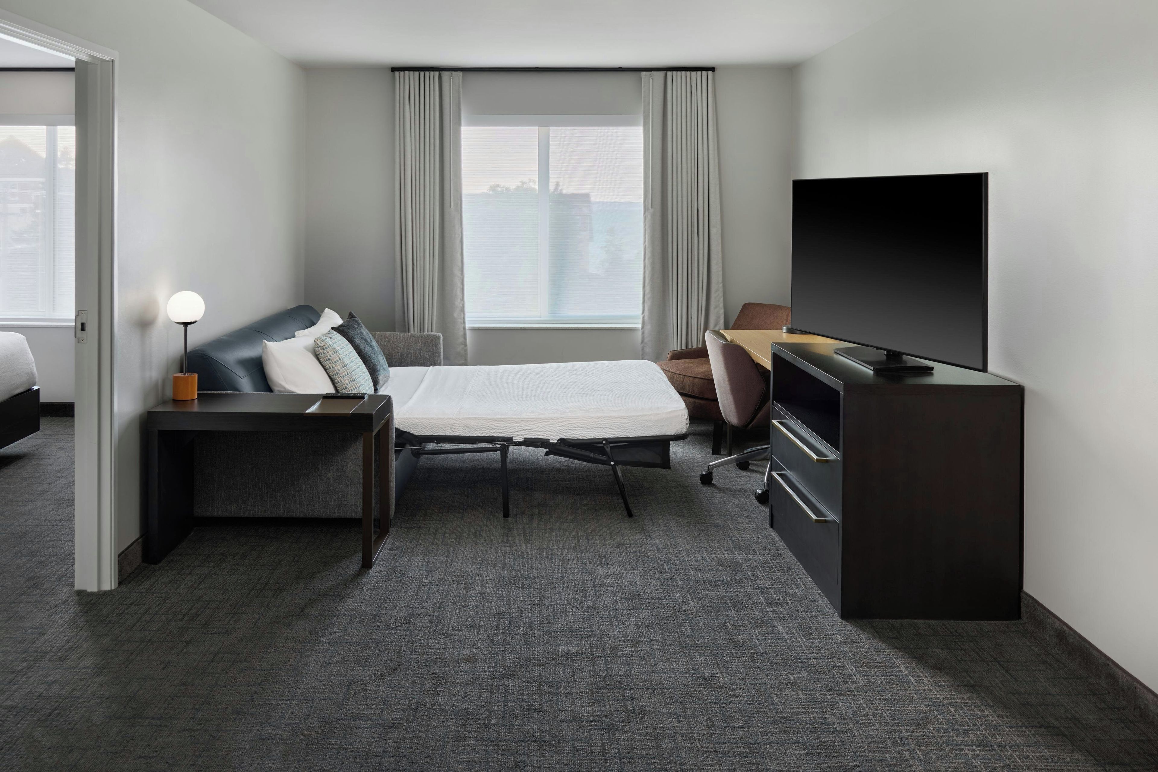 Une chambre d’hôtel avec un lit, un bureau, une chaise, une télévision et une fenêtre avec des rideaux.