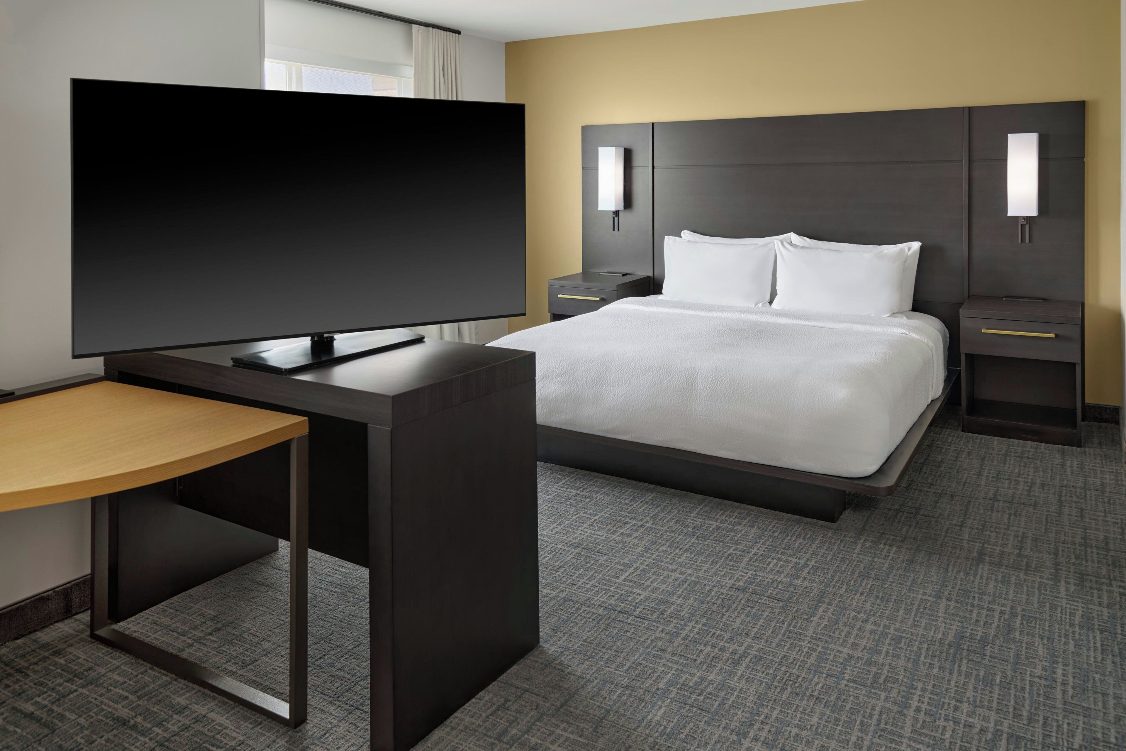 A hotel room with a bed, a desk with a flat-screen TV, and bedside tables.
