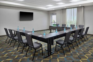 A conference room with a long table, chairs, water bottles, a flat-screen TV, and a window with curtains.