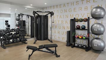 Un gimnasio con equipo de ejercicio variado, incluyendo mancuernas, pesas rusas y un banco.
