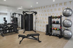 Un gimnasio con equipo de ejercicio variado, incluyendo mancuernas, pesas rusas y un banco.