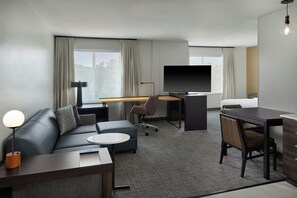 Ein Hotelzimmer mit einer Couch, einem Schreibtisch, einem Fernseher und einem Bett.