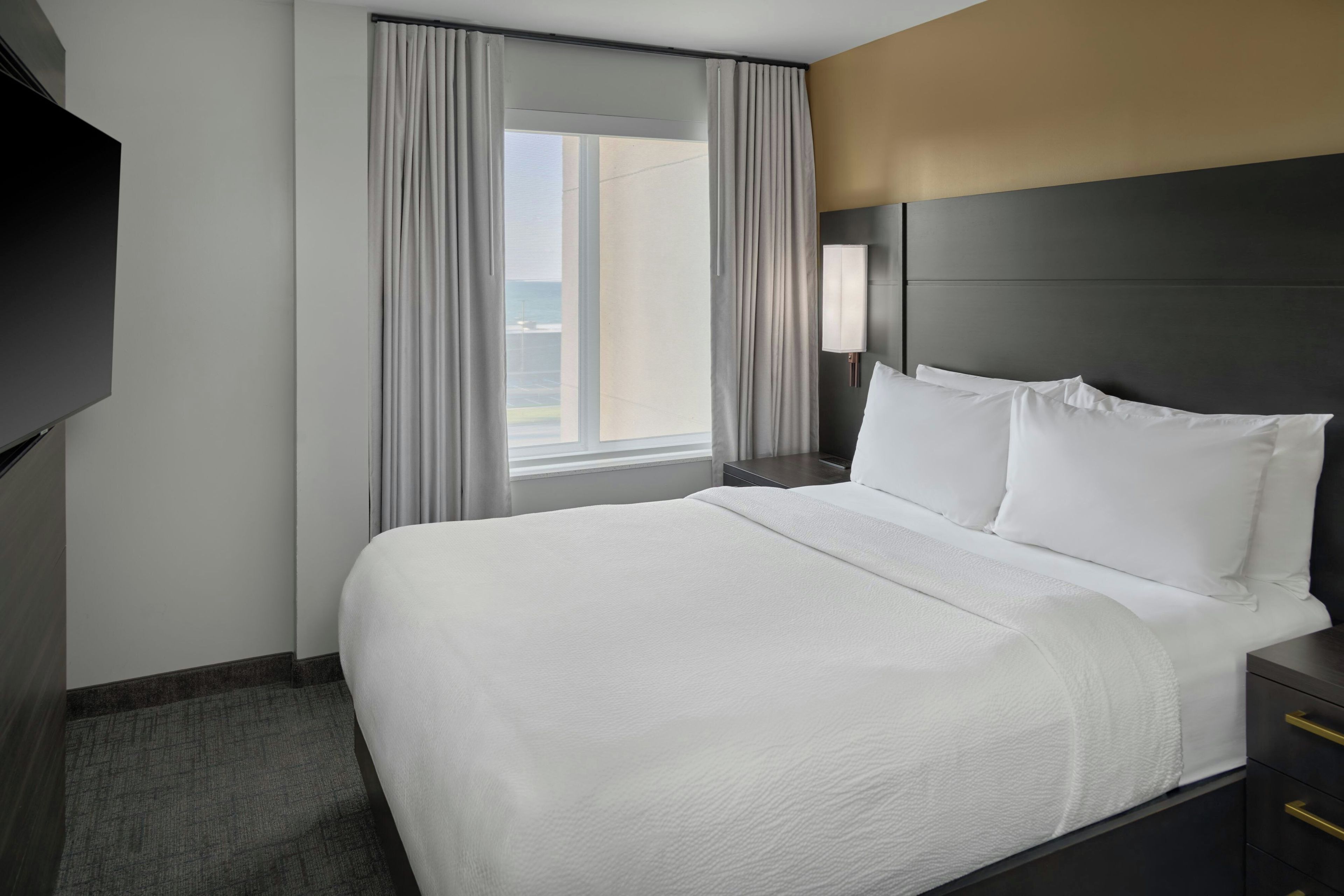 A hotel room with a large bed, a nightstand, a lamp, and a window with curtains.
