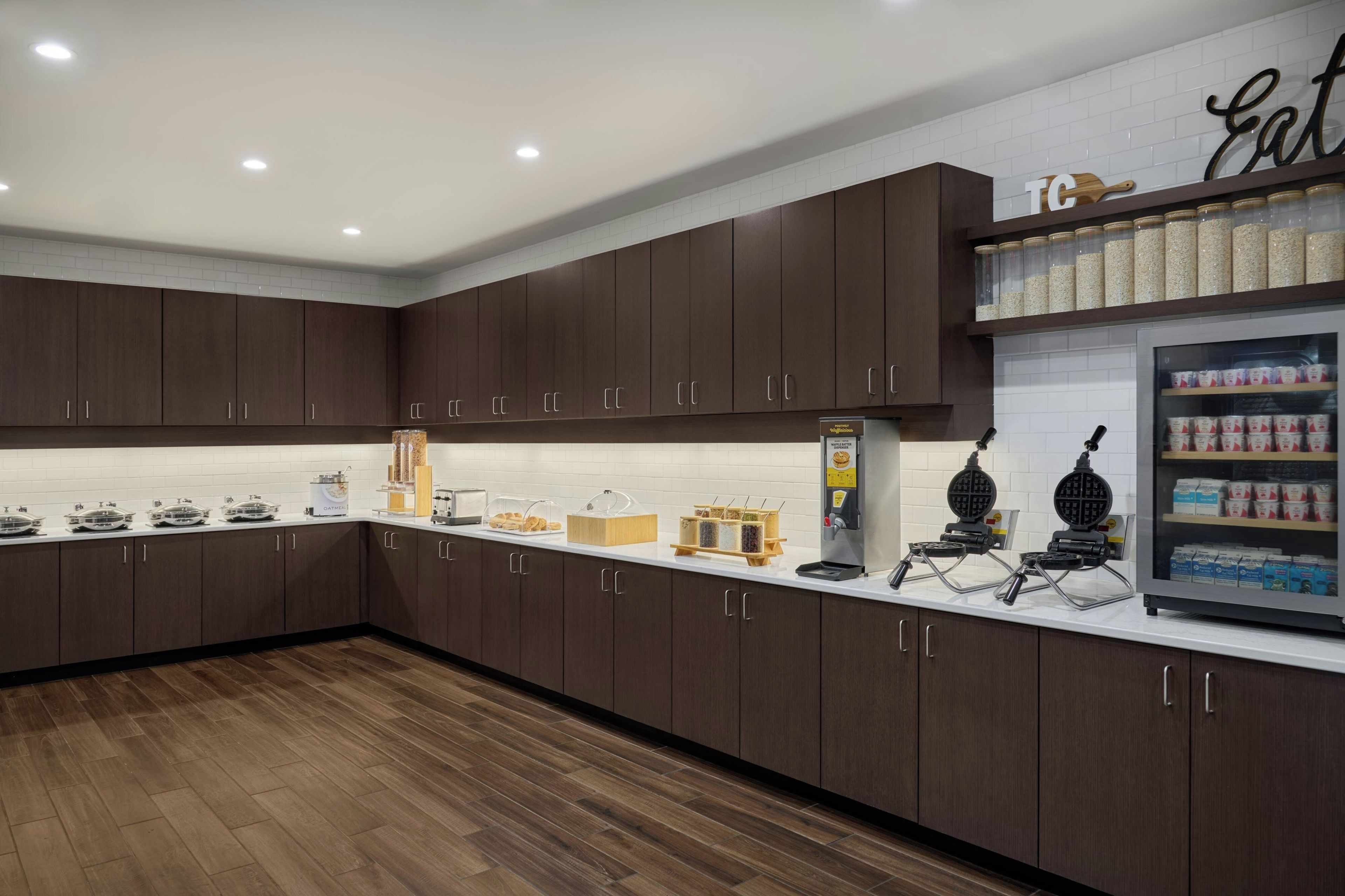 A modern kitchen with dark wood cabinets, a white countertop, and a waffle maker.