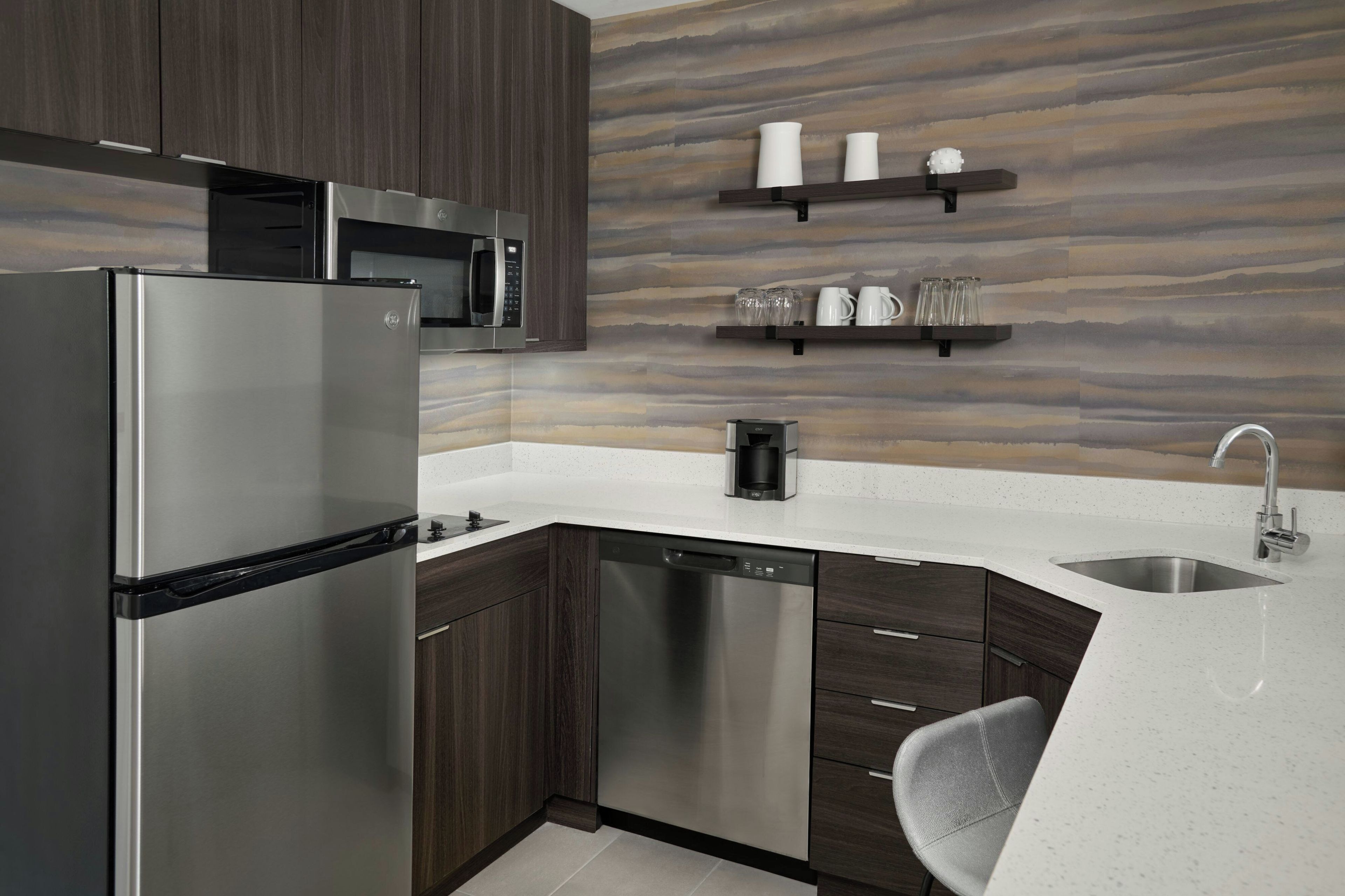 Cocina moderna con refrigerador de acero inoxidable, lavavajillas y microondas. Hay una cafetera en la encimera y un lavatorio con grifo.