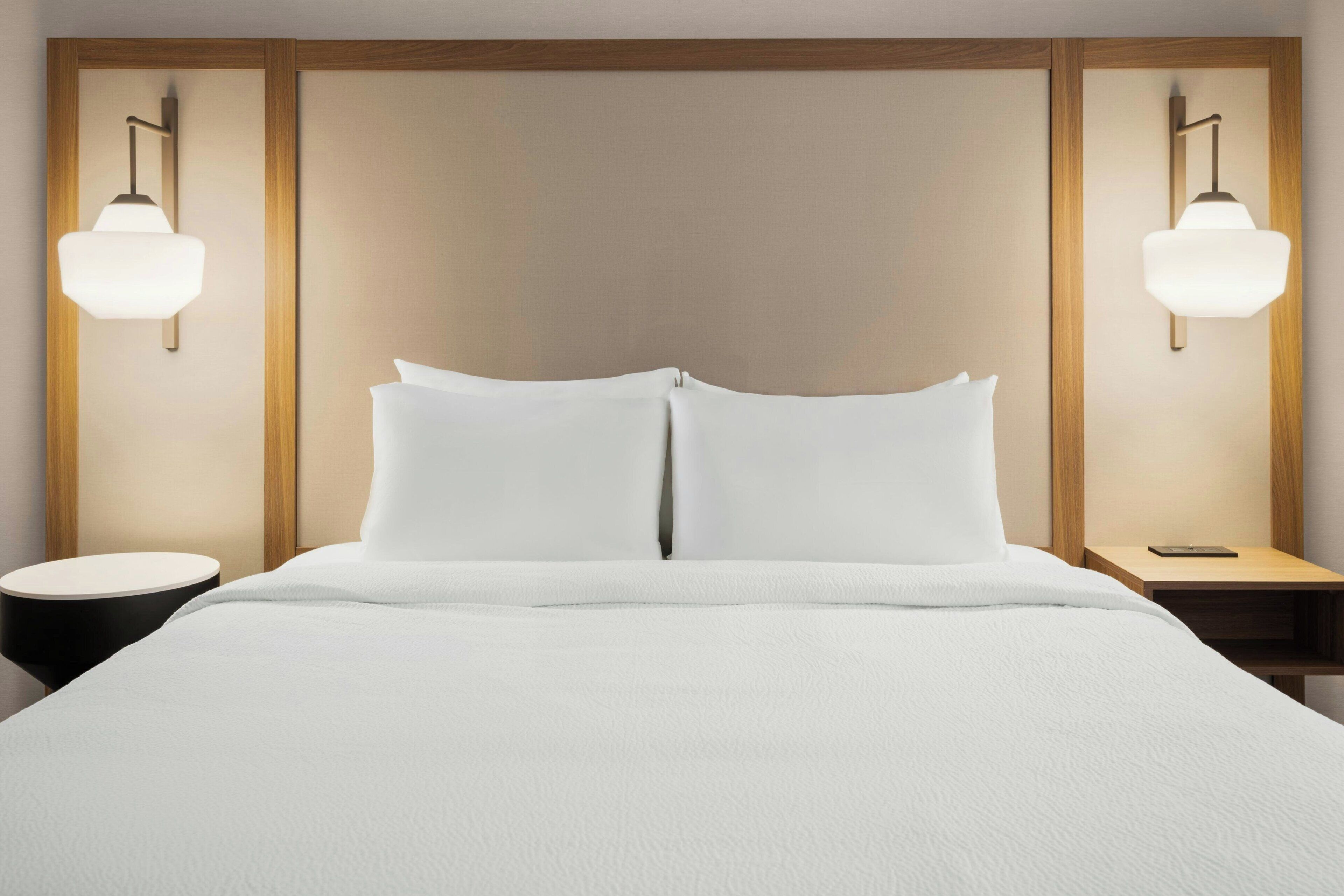 A hotel room with a large bed, two bedside tables, and wall-mounted lamps.