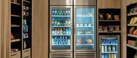 Un espace commercial où l’on trouve des étagères réfrigérées remplies de boissons et d’en-cas.