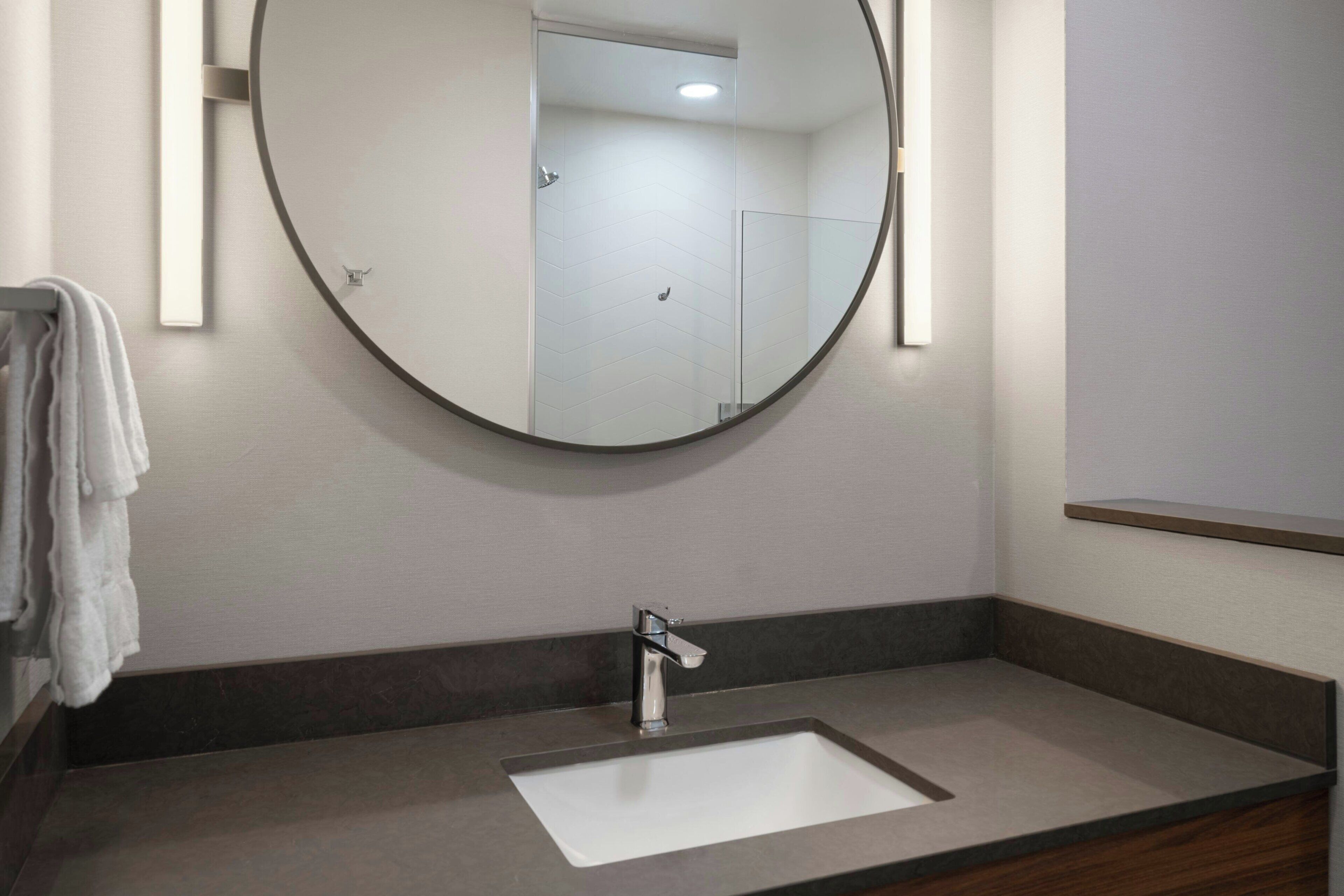 Une salle de bain avec un miroir rond, un lavabo rectangulaire et un porte-serviettes.