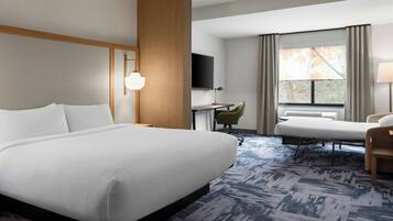 A hotel room with a large bed, a desk, a chair, a TV, and a window with curtains.
