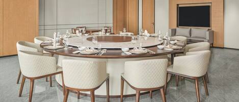 A modern conference room with a round table, white chairs, and a large screen.