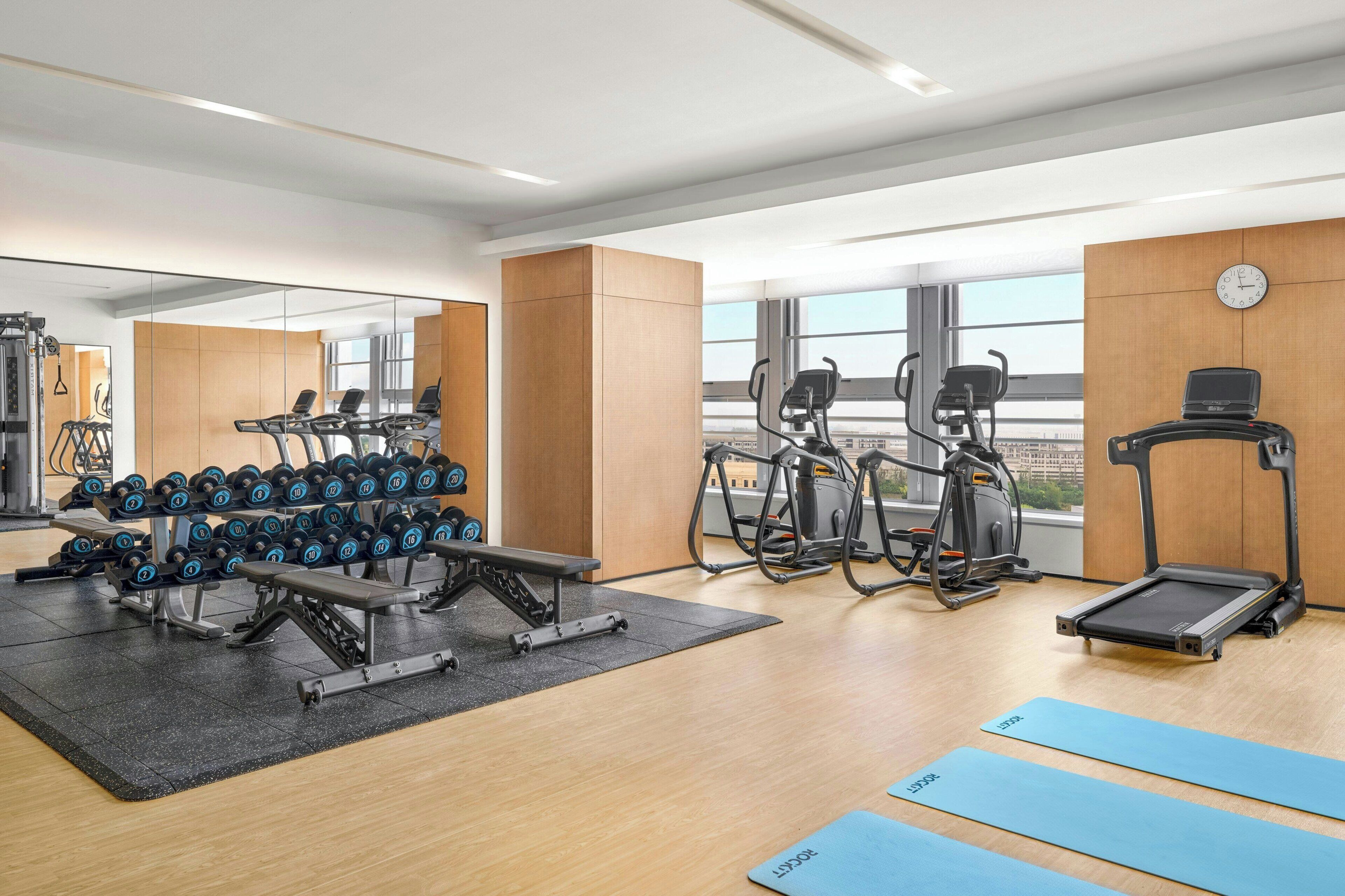A modern gym with exercise equipment, a mirror, and large windows.