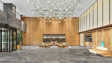 Un hall d’entrée spacieux au design moderne, comprenant un espace détente avec des canapés et des fauteuils, un grand mur recouvert de panneaux en bois et un luminaire au plafond au design original.