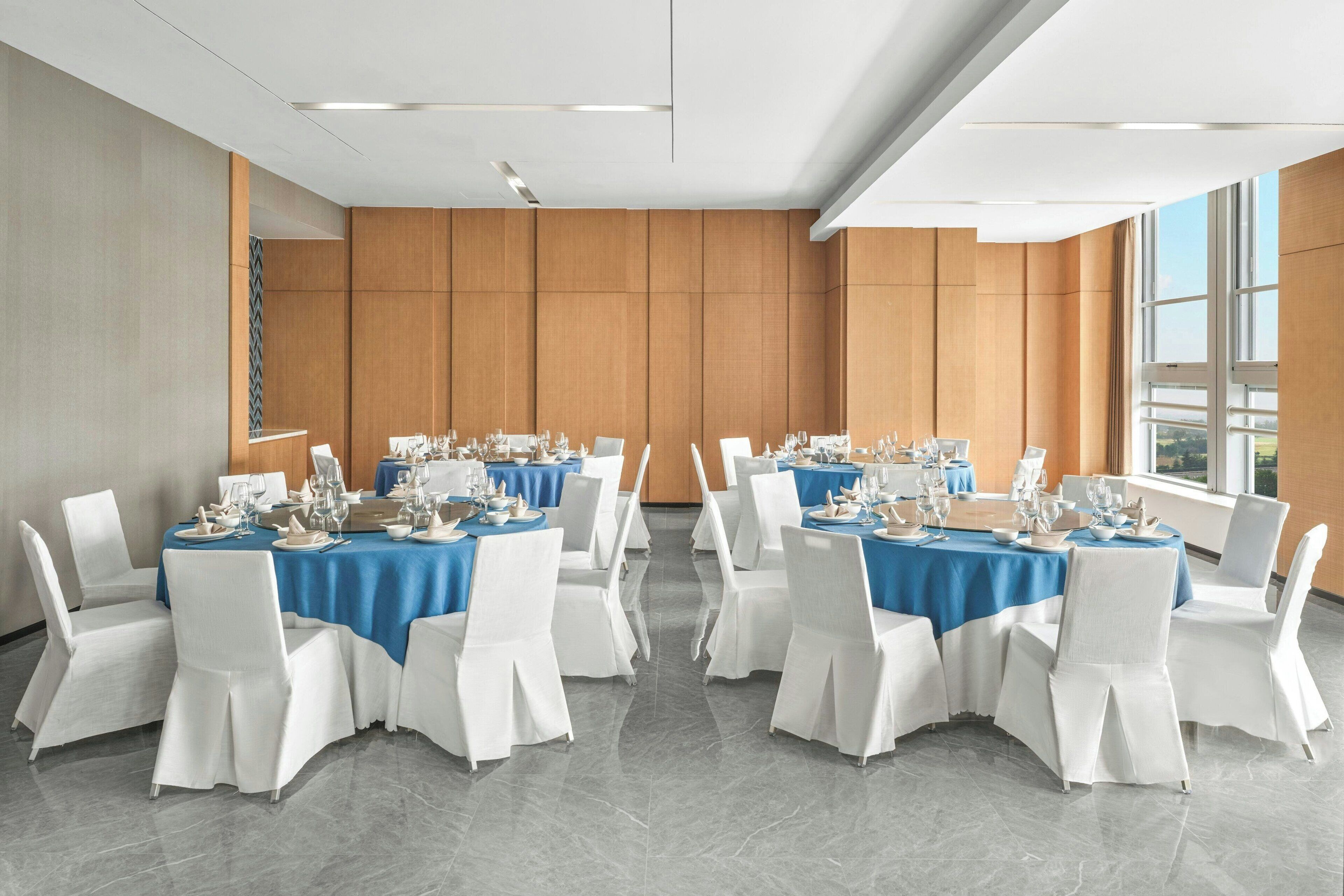 Un salón de conferencias con mesas redondas, sillas blancas y manteles azules.