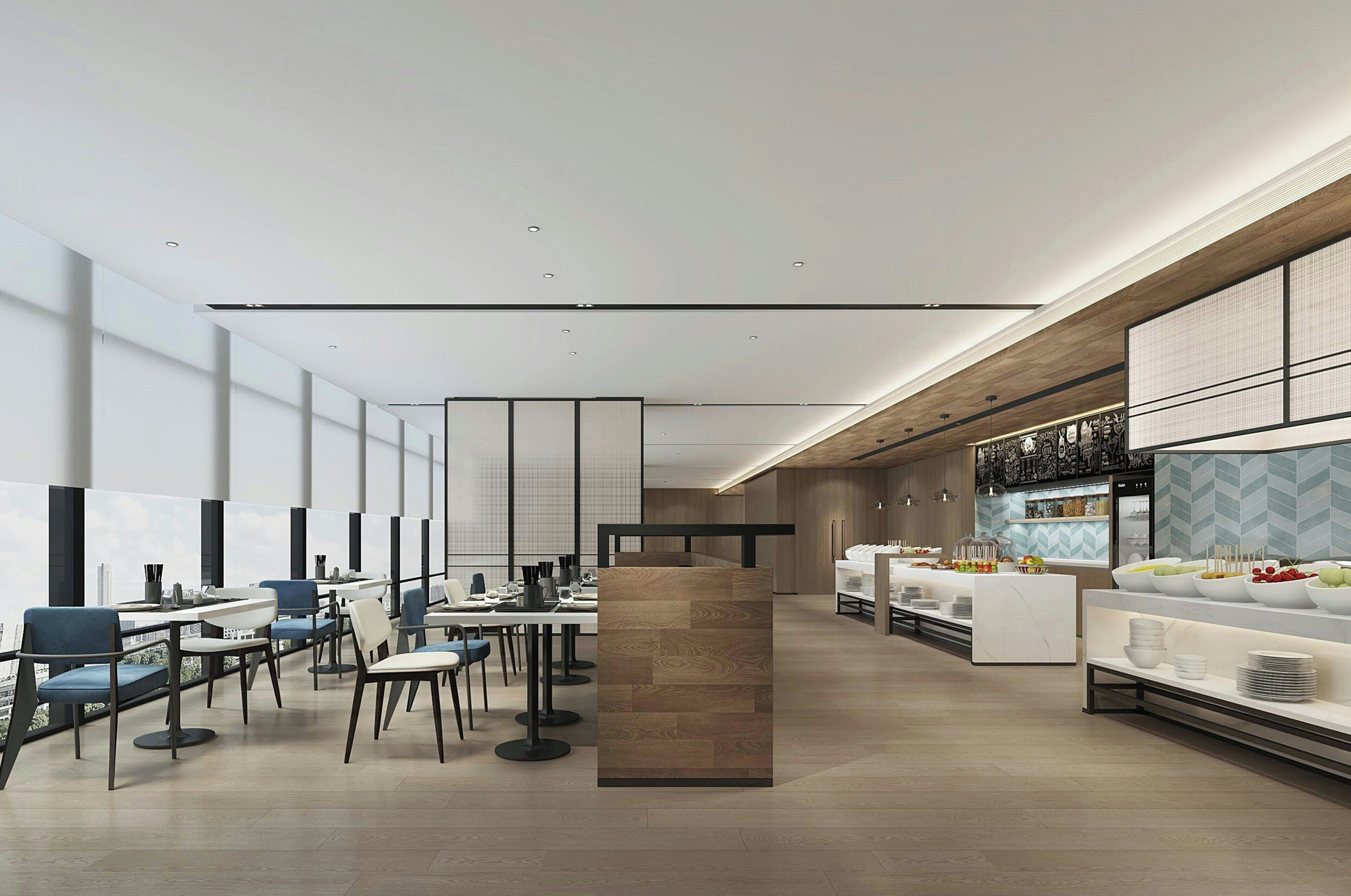 A modern hotel lobby with a long reception desk, seating area with tables and chairs, and a buffet counter with food displays.