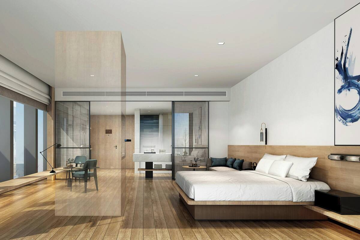 Une chambre moderne avec un grand lit, un bureau et une chaise. On peut apercevoir la salle de bain à travers une porte en verre.