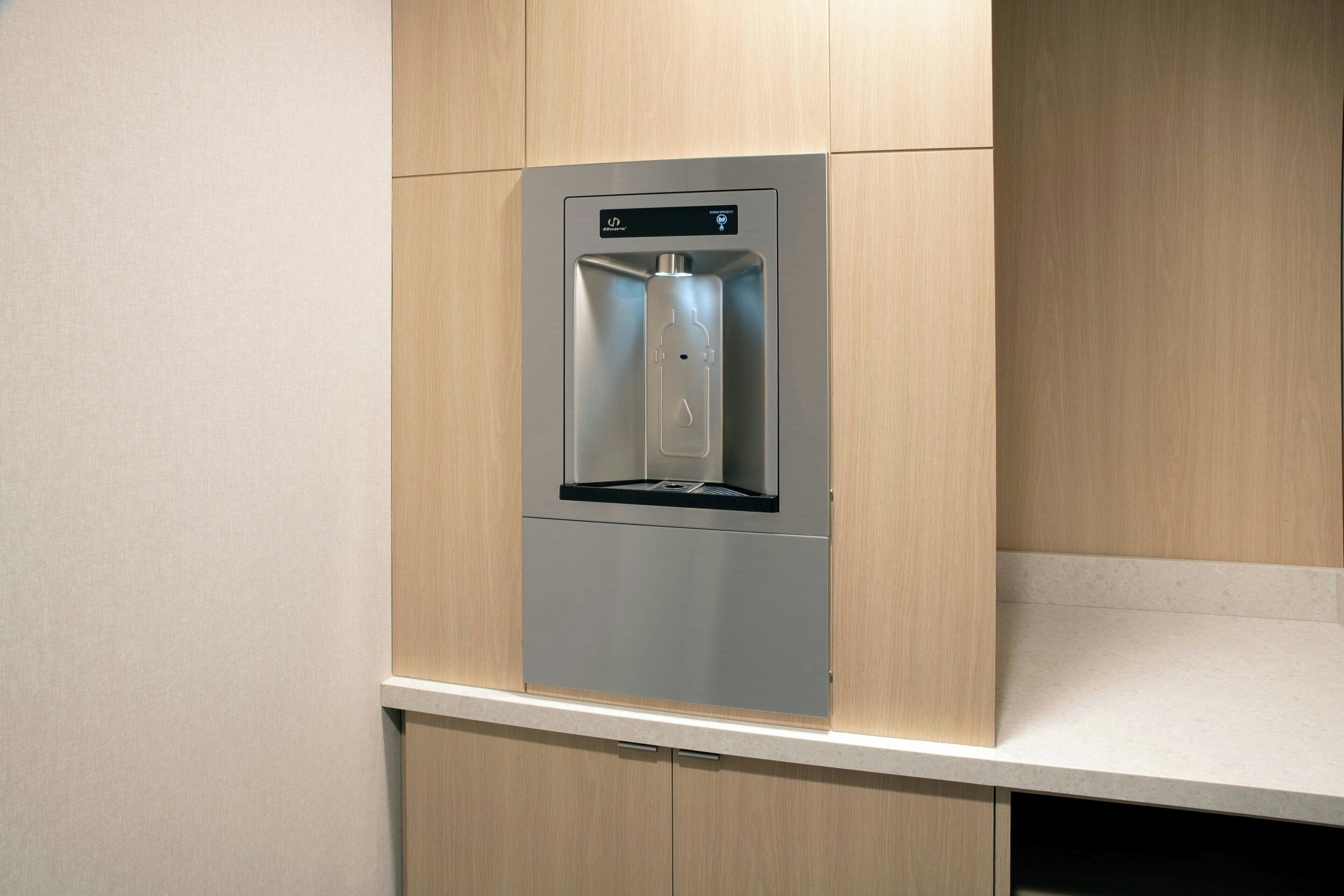 A stainless steel water dispenser integrated into a wooden cabinet with a countertop below.