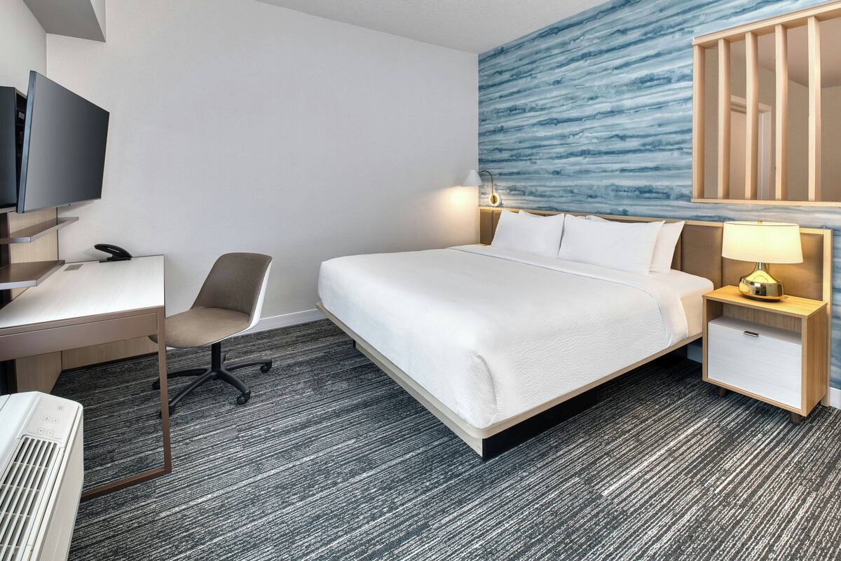 Una habitación de hotel con cama, escritorio, silla, televisión y una pared con diseño abstracto azul.