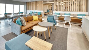 Un moderno espacio lounge con sofás, mesas y sillones, que cuenta con un ventanal grande y un separador de madera.