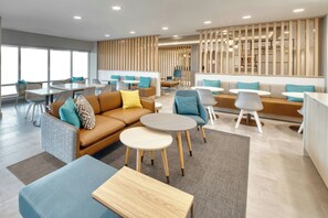 Un moderno espacio lounge con sofás, mesas y sillones, que cuenta con un ventanal grande y un separador de madera.