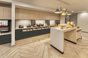 A modern kitchen with wooden cabinets, a central island, and a digital menu display.