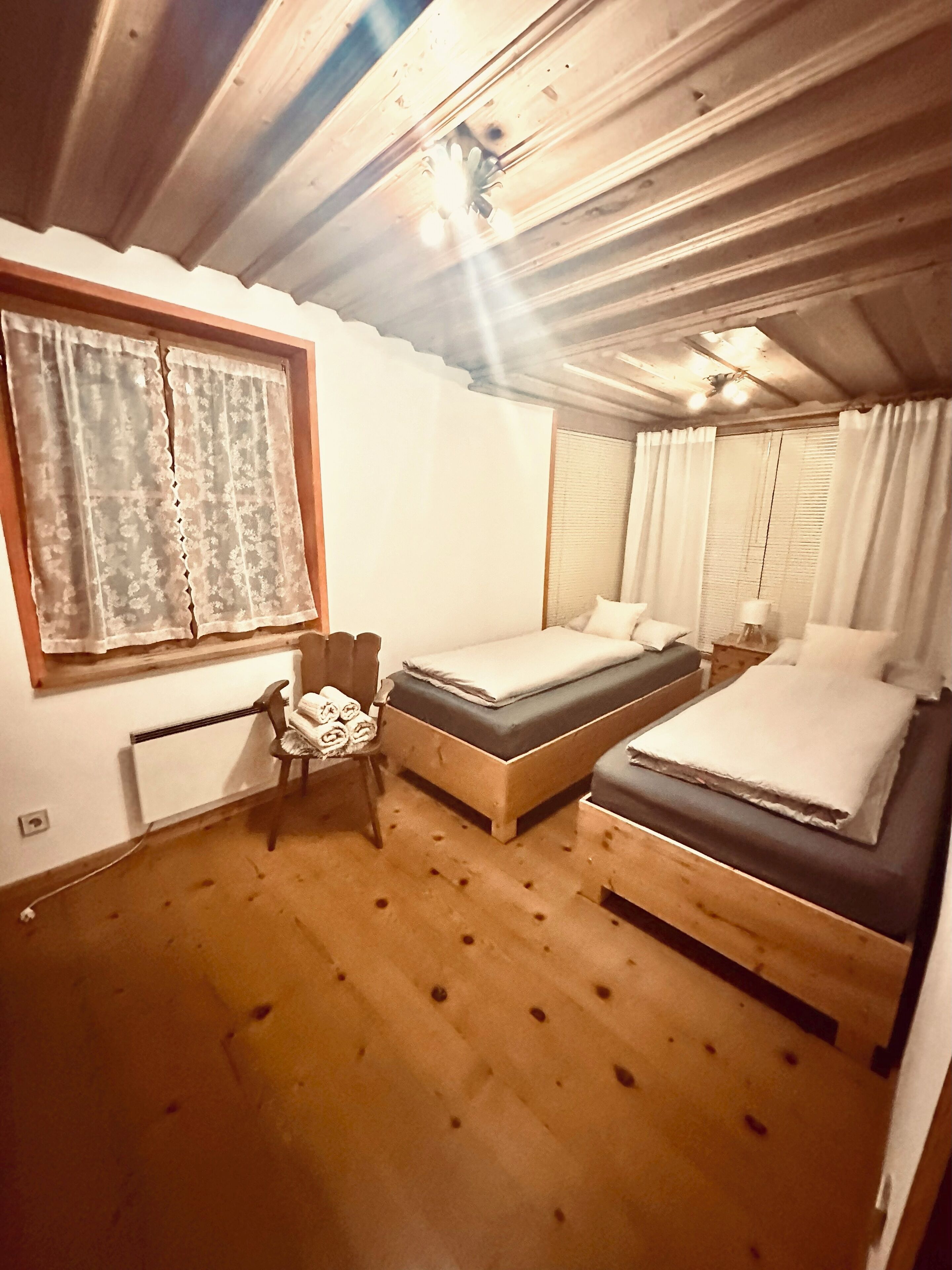 Une chambre avec deux lits, une chaise, un radiateur et une fenêtre avec des rideaux.