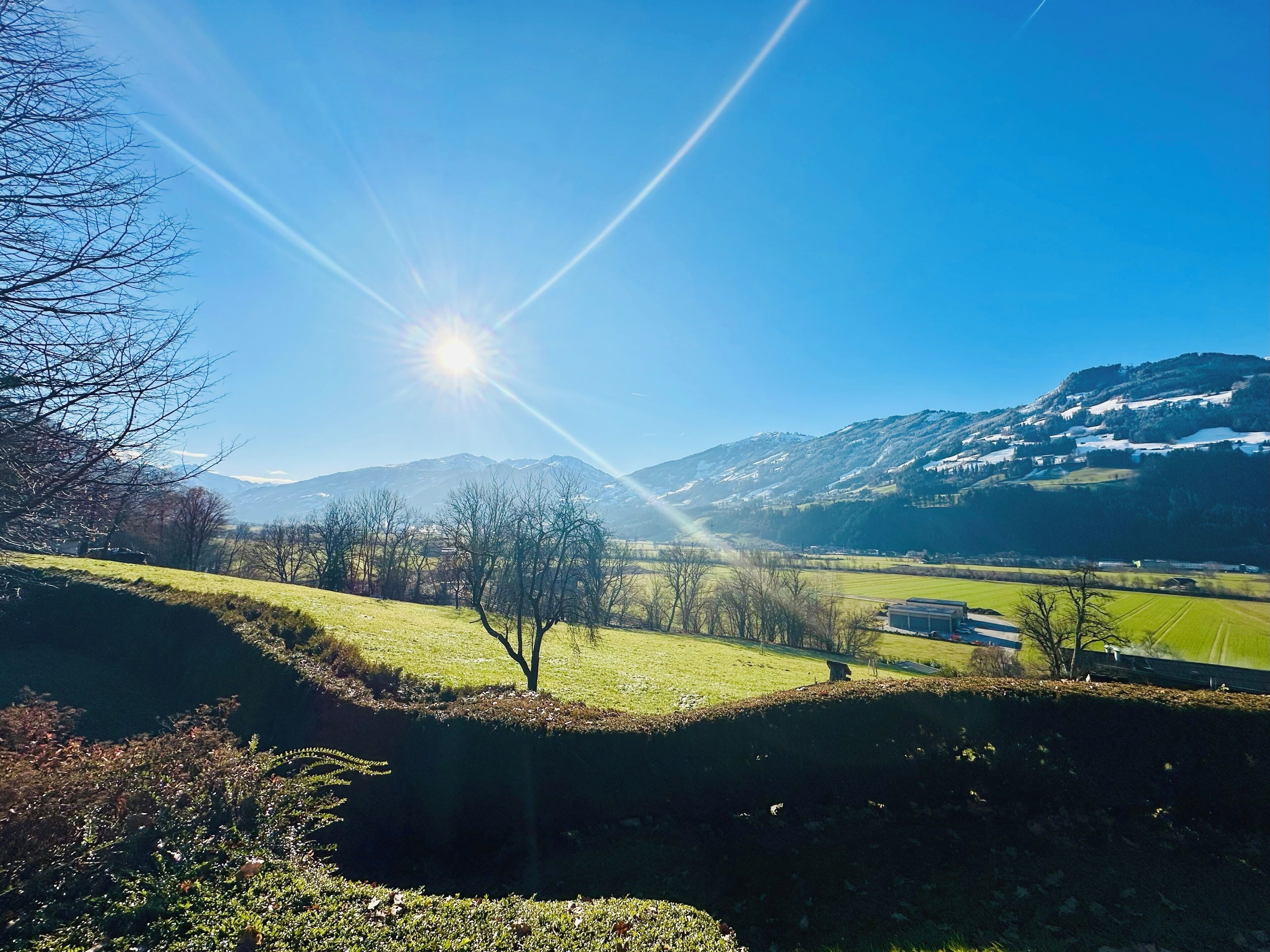 Un paysage rural avec un ciel dégagé, un soleil brillant et des montagnes en arrière-plan.